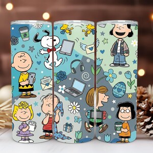 Könnte beinhalten: Drei Edelstahlbecher mit einem Cartoon-Design mit Charakteren aus dem Peanuts-Comicstrip. Die Becher haben einen hellblauen Hintergrund mit verschiedenen Illustrationen von Snoopy, Charlie Brown und anderen Charakteren.