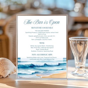 May include: A clear acrylic bar menu displaying "The Bar is Open" in script. It details cocktails, wines, and non-alcoholic options. The bottom features a watercolour beach scene. A seashell and a glass are in the foreground.