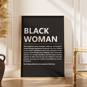 以下が含まれることがあります： 黒い背景と金色のフレームの額入りアートプリント。「BLACK WOMAN」の文字が大きな白い文字で上部に表示され、その後にモチベーションを高めるメッセージが続きます。左側には、乾燥した植物が入った装飾的な花瓶があります。