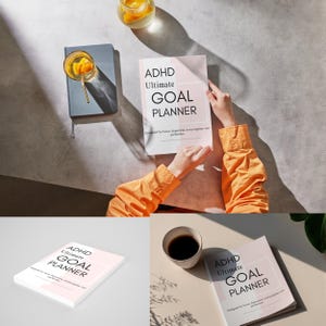 May include: A white and pink ADHD Ultimate Goal Planner with the text "ADHD Ultimate GOAL PLANNER" is held open by a person wearing an orange shirt. A gray notebook and a glass of orange-infused water are also visible.