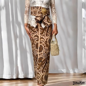 May include: A traditional Indonesian outfit featuring a long, patterned skirt in shades of brown and beige. The outfit includes a white lace top with long sleeves, a decorative belt, and a small woven handbag. The outfit is suitable for special occasions.