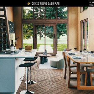 May include: A 26'x30' prefab cabin plan interior featuring a kitchen island with black stools, a dining area with a glass-top table and wooden chairs, and a living space with a curved sofa. Large windows overlook a green outdoor area.