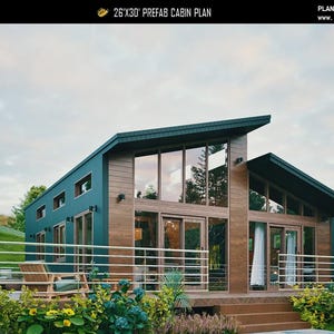 May include: A 26'x30' prefab cabin plan labeled C-25-109. The structure features a dark teal metal exterior, wood-paneled accents, and large floor-to-ceiling windows. A metal railing surrounds the front deck, which includes a wooden chair.