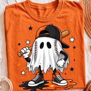 May include: An orange t-shirt featuring a graphic of a ghost shaped like a baseball, wearing a black and orange baseball cap and high-top sneakers. The ghost holds a wooden baseball bat, surrounded by small black, white, and orange stars.