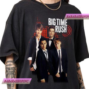 Könnte beinhalten: Dunkelgraues T-Shirt mit einer Grafik der Band Big Time Rush. Das Bild zeigt vier Männer in Anzügen mit dem Namen der Band in weißem Text und einem roten Design. Das Shirt ist ein lässiger Stil.