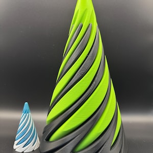 May include: Two decorative cone-shaped objects. The larger cone is green and black, with a spiral design. The smaller cone is blue and white, also with a spiral design. Both objects are on a black surface.