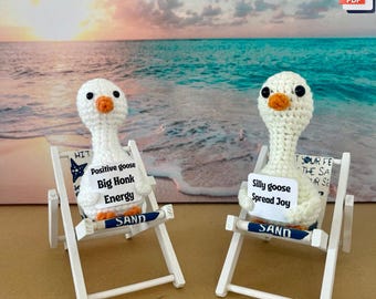 May include: Two crochet goose figurines in beach chairs. One reads "Positive goose Big Honk Energy", the other "Silly goose Spread Joy". The chairs are white with blue accents, set against a beach scene. The words "Crochet pattern" are at the bottom.