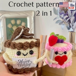 Op de afbeelding: Twee gehaakte cake-vormige items. Eén is crèmekleurig met een chocoladekoekje en een bordje met de tekst "Happy Birthday!". De andere is roze en crème met een rood hart en een aardbei. De tekst "Crochet pattern 2 in 1" staat bovenaan.