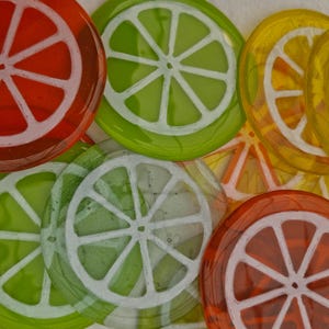 May include: A selection of colourful glass coasters shaped like citrus fruit slices. The coasters display vibrant colours such as red, green, and yellow, with white segmented designs. These decorative coasters add a refreshing touch to any home decor.