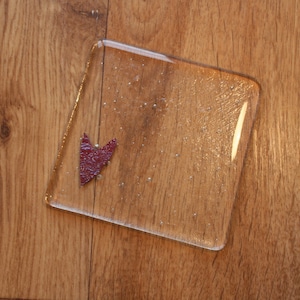 May include: A clear glass coaster with a small, red heart-shaped piece of paper on top.