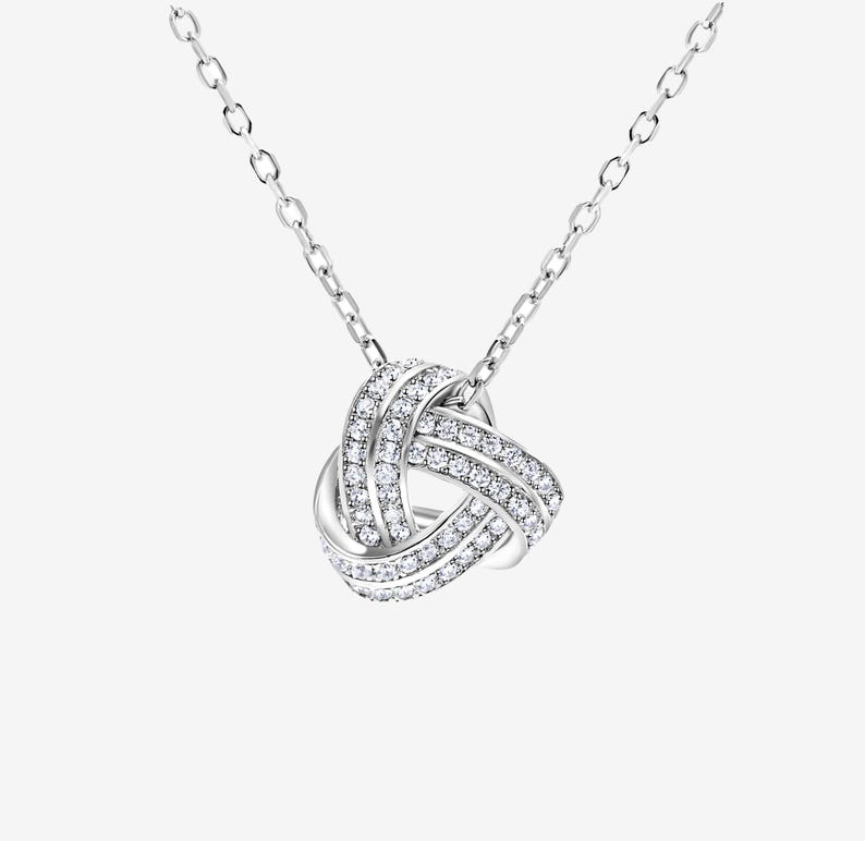 May include: A silver necklace with a knot-shaped pendant encrusted with clear cubic zirconia stones.