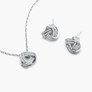 May include: A silver necklace and earrings set with a knot design and clear cubic zirconia stones.