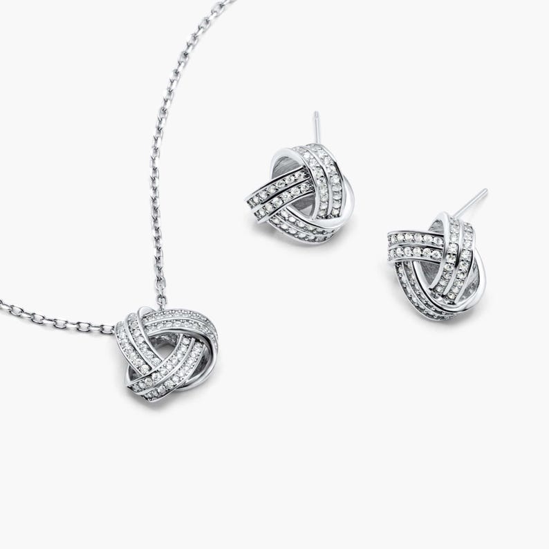 May include: A silver necklace and earrings set with a knot design and clear cubic zirconia stones.
