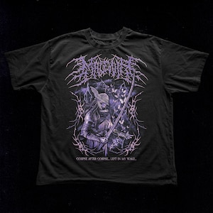 May include: Black t-shirt featuring a detailed graphic of a warrior holding a sword, with the text "MAGNIFIER" above and "CORPSE AFTER CORPSE... LEFT IN MY WAKE..." below. The design incorporates purple and white accents, creating a striking visual.