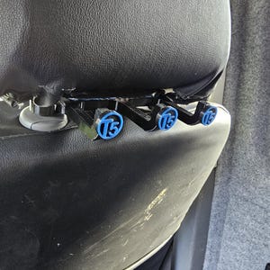 Puede incluir: Reposacabezas de asiento de coche negro con tres accesorios negros y azules. Cada accesorio tiene un círculo azul con el número "15" en blanco. El reposacabezas está hecho de material negro similar al cuero.