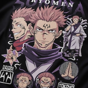 Puede incluir: Camiseta negra con un diseño gráfico de un personaje con pelo rosa y marcas faciales. El diseño incluye el texto "RYOMEN" y "JUJUTSU KAISEN" junto con otros textos e imágenes japoneses.