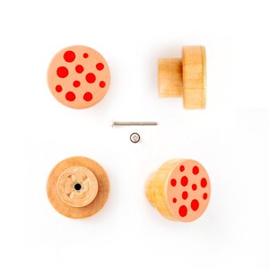 Puede incluir: Cuatro pomos de madera con lunares rojos. Los pomos son redondos y tienen un pequeño agujero en el centro para un tornillo. Los pomos están sobre un fondo blanco.