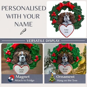 Puede incluir: Un artículo decorativo con la cabeza de un Cavalier King Charles Spaniel marrón y blanco dentro de una corona de acebo verde con un lazo rojo y bayas rojas. Debajo cuelga una placa blanca en forma de corazón con nombres como Lucy, Duke o Blue y 2026.