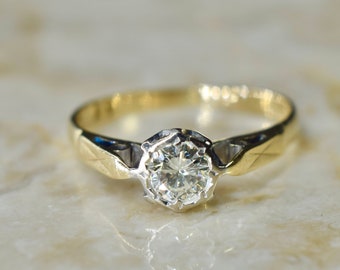 Puede incluir: Un anillo de oro con un solo diamante redondo engastado en un engaste de metal blanco. La banda es ligeramente curvada y tiene un acabado texturizado.