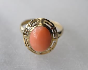 May include: A gold ring with a coral stone set in a geometric design.