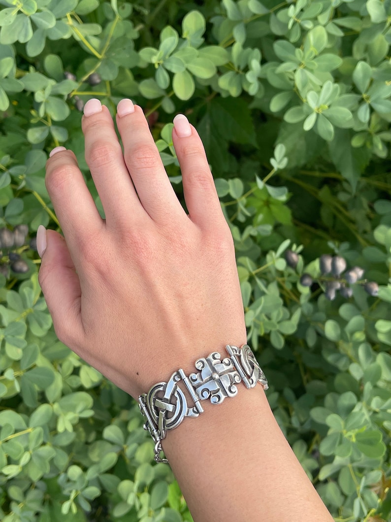 May include: A silver bracelet featuring a detailed, intricate design. The bracelet is made up of linked, interlocking pieces with a geometric pattern.