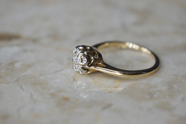 May include: A gold ring with a round, white diamond center stone surrounded by smaller diamonds. The ring has a delicate, intricate design.
