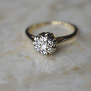 May include: A gold ring with a cluster of small diamonds set in a flower-shaped design.