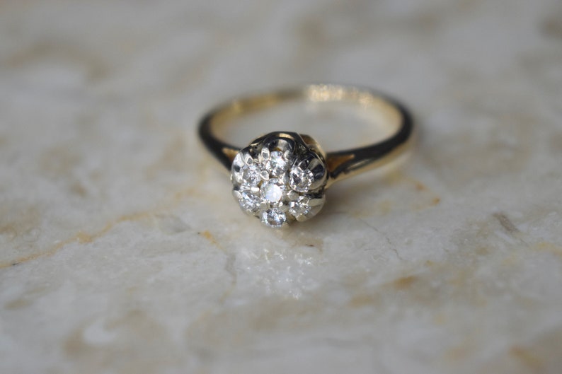 May include: A gold ring with a cluster of small diamonds set in a flower-shaped design.