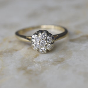 May include: A gold ring with a cluster of small diamonds set in a flower-shaped design.