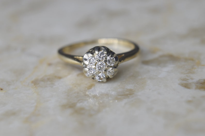 May include: A gold ring with a cluster of small diamonds set in a flower-shaped design.