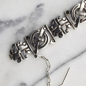 May include: A silver bracelet with a chain and clasp. The bracelet is made of interlocking circles and features a Celtic knot design.