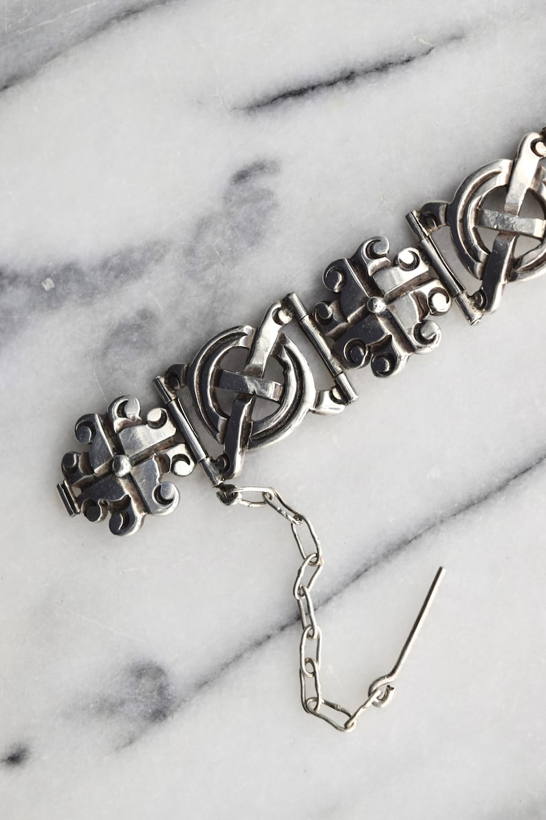 May include: A silver bracelet with a chain and clasp. The bracelet is made of interlocking circles and features a Celtic knot design.