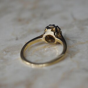 May include: A gold ring with a single round gemstone set in a prong setting. The ring is on a white marble surface.