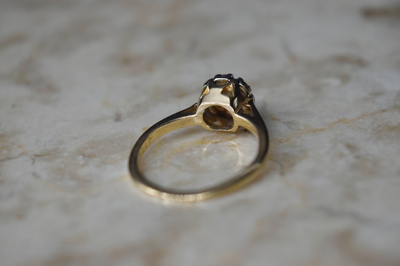 May include: A gold ring with a single round gemstone set in a prong setting. The ring is on a white marble surface.