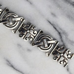 May include: A silver bracelet with a detailed, intricate design. The bracelet is made up of repeating links, each featuring a circular motif with a cross in the centre.