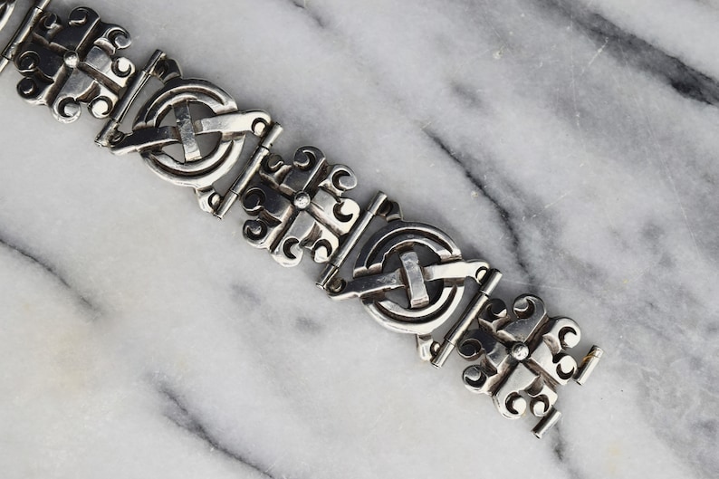 May include: A silver bracelet with a detailed, intricate design. The bracelet is made up of repeating links, each featuring a circular motif with a cross in the centre.