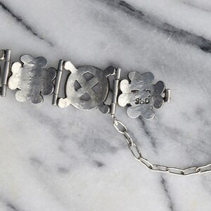 May include: A silver bracelet with a chain and a clasp. The bracelet is made of interlocking circles with a cross design. The clasp is stamped with the number "925".