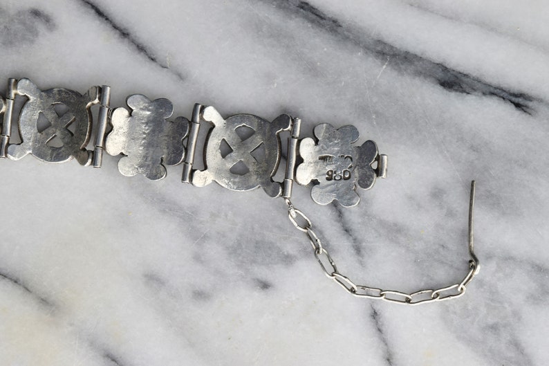 May include: A silver bracelet with a chain and a clasp. The bracelet is made of interlocking circles with a cross design. The clasp is stamped with the number "925".