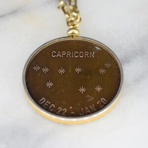 May include: A gold-toned Capricorn pendant with a constellation design. The pendant features the word "CAPRICORN" at the top, with star symbols below. The dates "DEC 22 - JAN 20" are inscribed at the bottom. The pendant is attached to a gold chain.