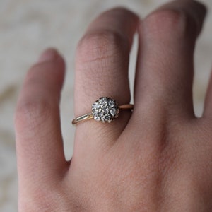 May include: A gold ring with a cluster of small diamonds set in a round shape.