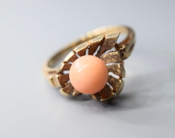 May include: A gold ring with a delicate, intricate design featuring a large, round, peach-colored gemstone.