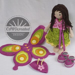May include: Crocheted butterfly wings, hat, and shoes in shades of pink, green, and yellow. A crocheted doll with brown hair and a green dress is standing next to the wings. The doll is wearing a pink cardigan and a pink ribbon around her waist. The image includes the text "CAROcreated DESIGN".