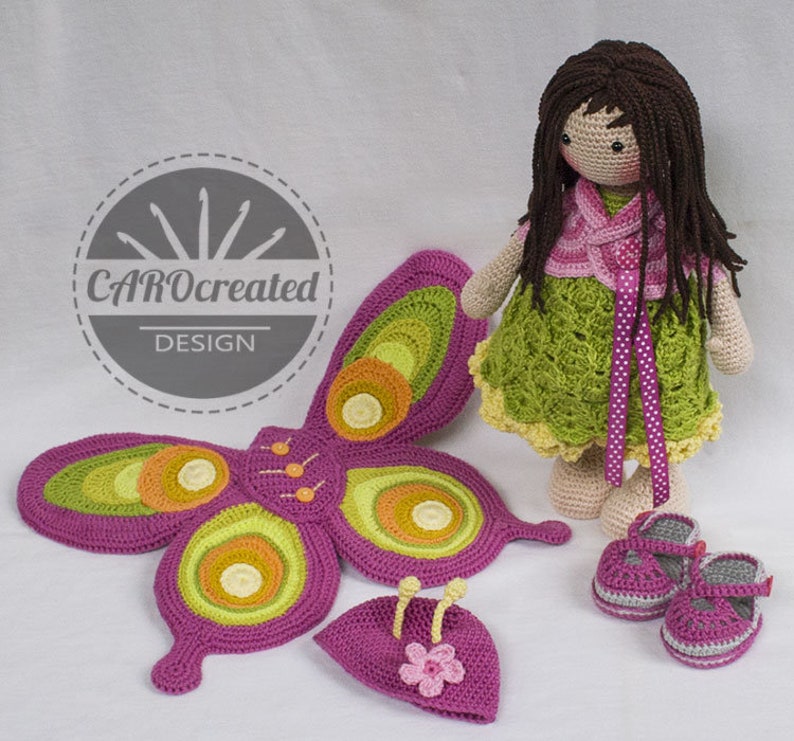 May include: Crocheted butterfly wings, hat, and shoes in shades of pink, green, and yellow. A crocheted doll with brown hair and a green dress is standing next to the wings. The doll is wearing a pink cardigan and a pink ribbon around her waist. The image includes the text "CAROcreated DESIGN".