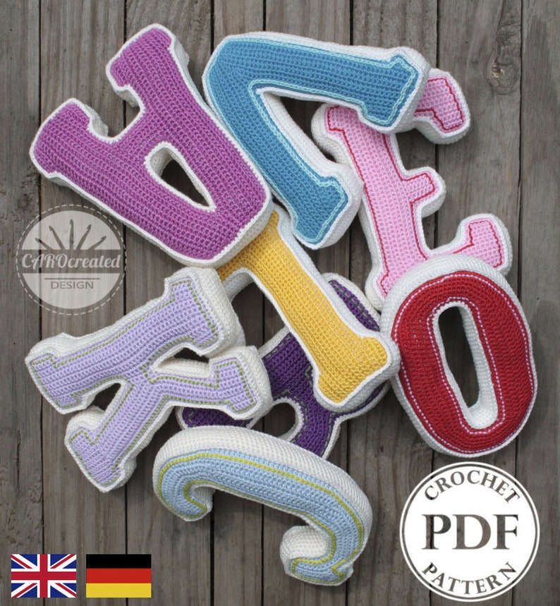 May include: A set of colorful crocheted letters, including H, A, T, K, I, O, and C, arranged on a wooden surface. The letters are made with different colored yarn, including purple, blue, pink, yellow, lavender, red, and light blue. The letters are outlined in white yarn. The letters are arranged in a pile, with the letter H on top. A white circle with the text "CROCHET PDF PATTERN" is in the lower right corner of the image.