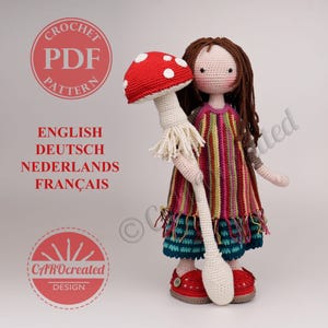 Könnte beinhalten: Eine Häkelpuppe mit langem braunem Haar, bekleidet mit einem gestreiften Kleid und einem blaugrünen Rock mit Fransen, hält einen großen rot-weißen Pilz. Der Text lautet: CROCHET PDF PATTERN, ENGLISH, DEUTSCH, NEDERLANDS, FRANÇAIS, CAROcreated DESIGN.