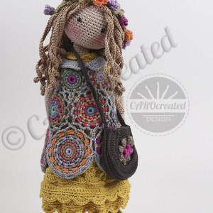 May include: A crocheted doll with long brown hair wearing a floral headband, a colorful crocheted dress, a brown crocheted purse, and brown shoes. The doll is standing on a white background.