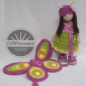 May include: A crocheted doll with long brown hair wearing a pink hat, green dress, and pink shoes. The doll is holding a pink and green butterfly with yellow and orange accents.