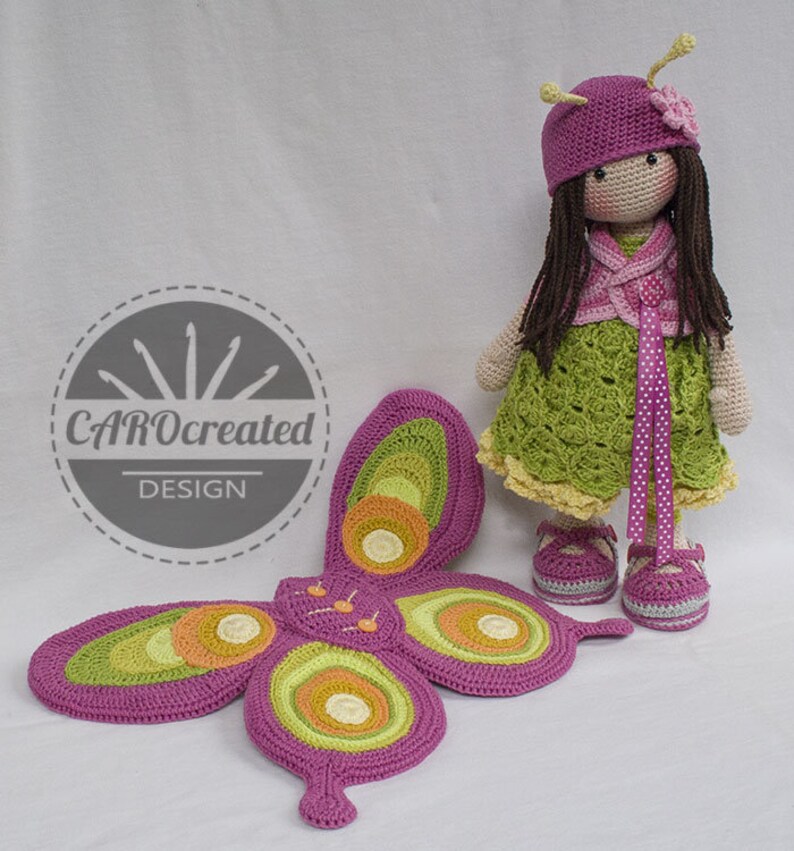 May include: A crocheted doll with long brown hair wearing a pink hat, green dress, and pink shoes. The doll is holding a pink and green butterfly with yellow and orange accents.