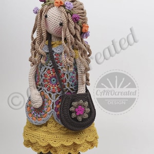 May include: Crocheted doll with long brown hair, wearing a yellow dress with a colorful crocheted vest, a brown bag with a pink flower, and a flower crown. The doll is wearing brown shoes.