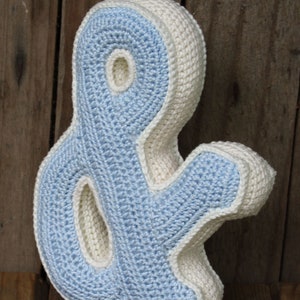 May include: A crocheted ampersand pillow in light blue and white. The pillow is shaped like the ampersand symbol and has a textured surface.